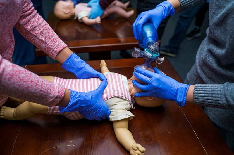 two healthcare staff carefully attach a ventilation device to a baby dummy as part of their PALS certification training